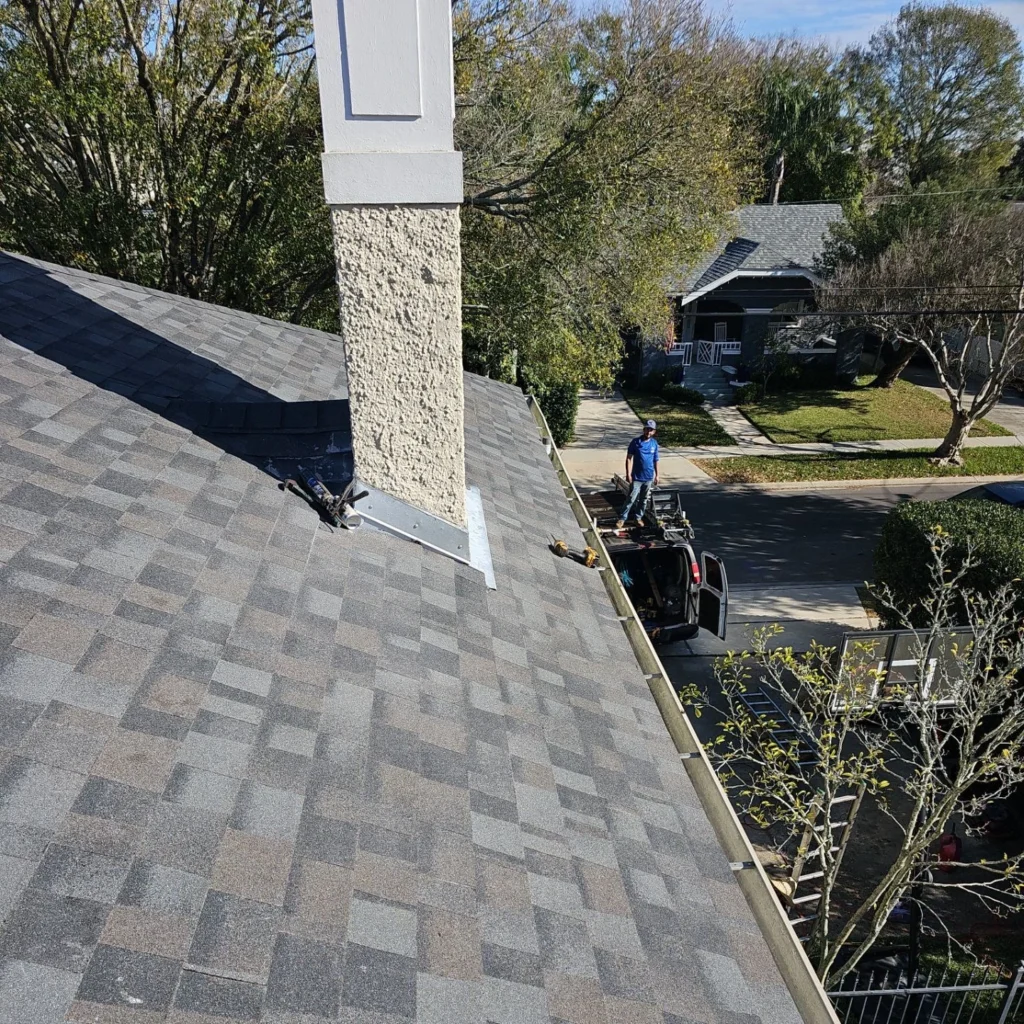 Fortified roof replacement with OC Williamsburg Gray architectural shingles, chimney flashing, and gutters on large Lakeview LA home.