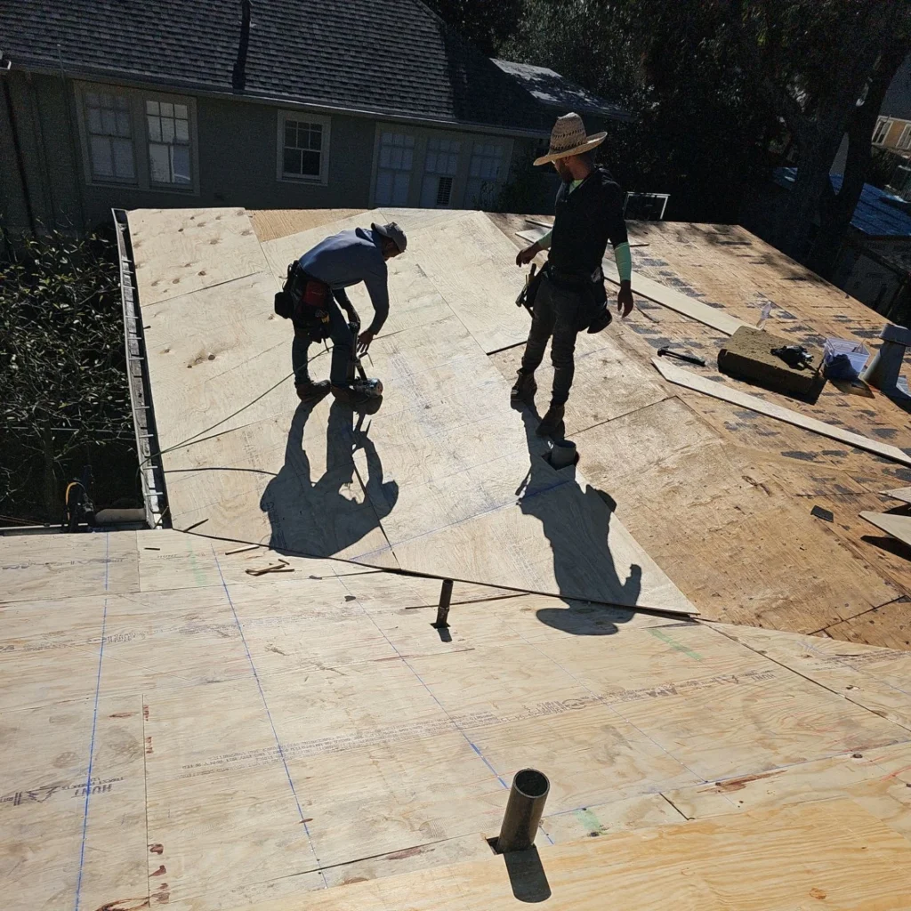 Two roofers installing plywood sheathing on large residential flat roof deck in Lakeview LA during FORTIFIED roof replacement.