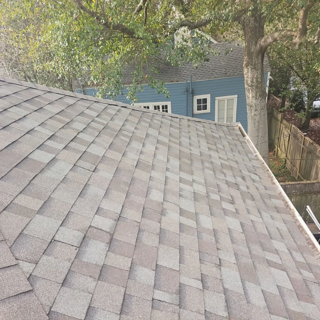 Owens Corning Driftwood architectural shingles on completed FORTIFIED roof replacement with gutter guards, historic blue home backdrop.