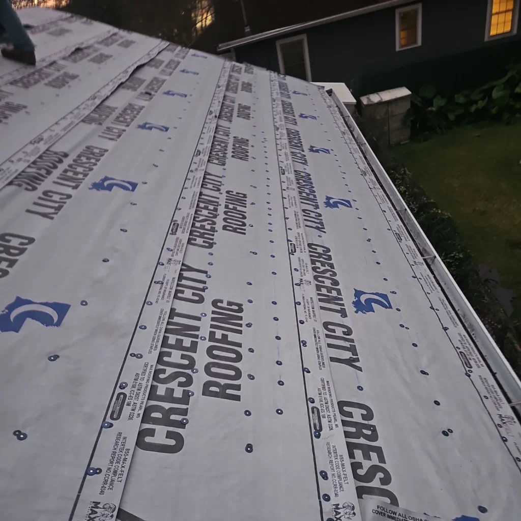 Crescent City Roofing underlayment installed across residential roof deck with cap nails, dusk setting, Kenner LA