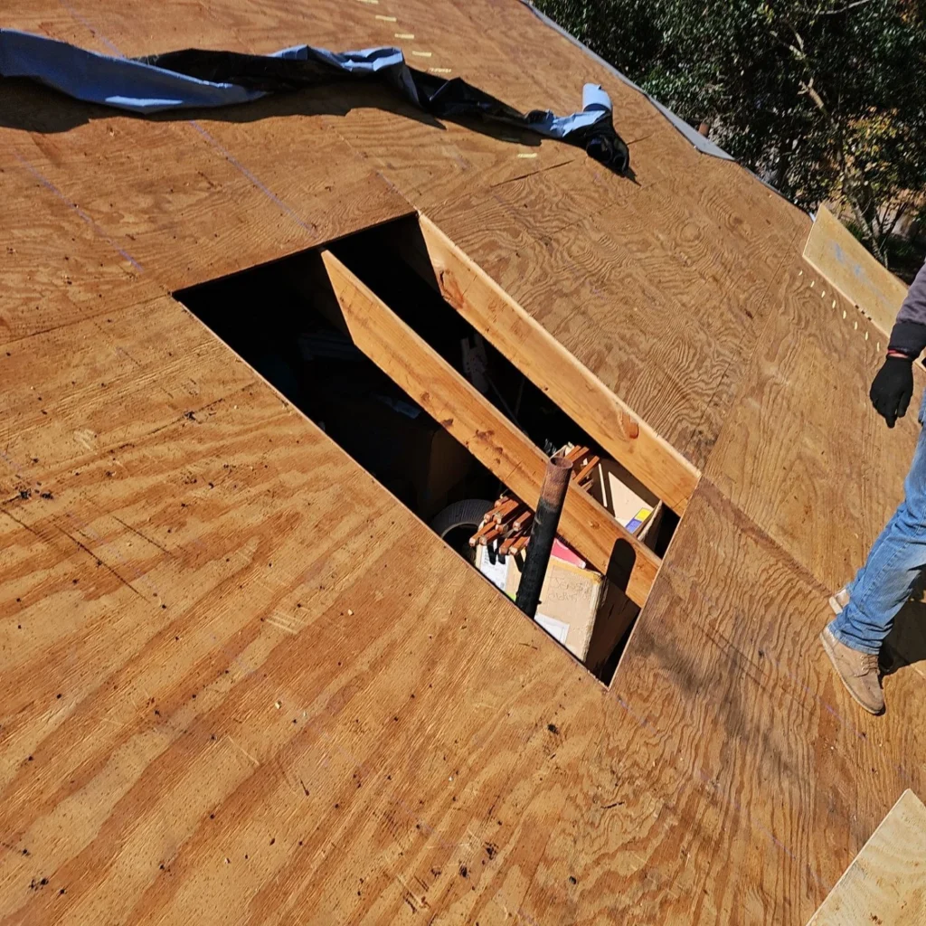 Roofer installs plywood sheathing on large residential roof with skylight framed opening visible below during Fortified roof replacement.