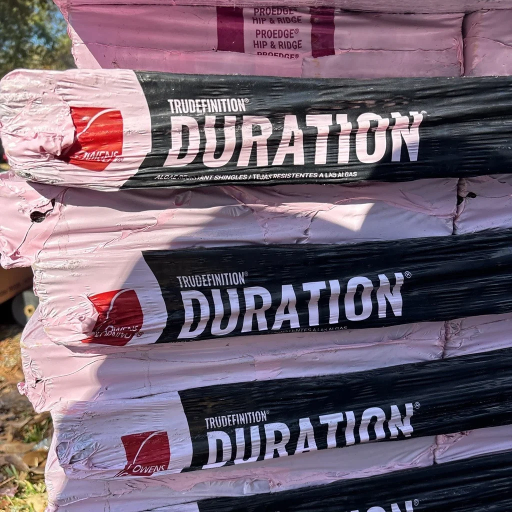 Stacked bundles of Owens Corning TruDefinition Duration algae-resistant shingles and ProEdge Hip & Ridge caps on a job site.