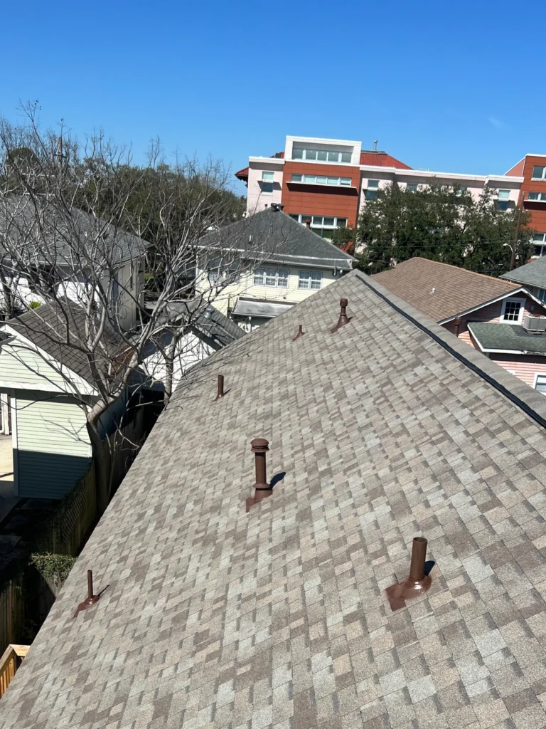Large residential roof replacement with OC Driftwood architectural shingles, multiple pipe boots, hip-style design, urban neighborhood setting.