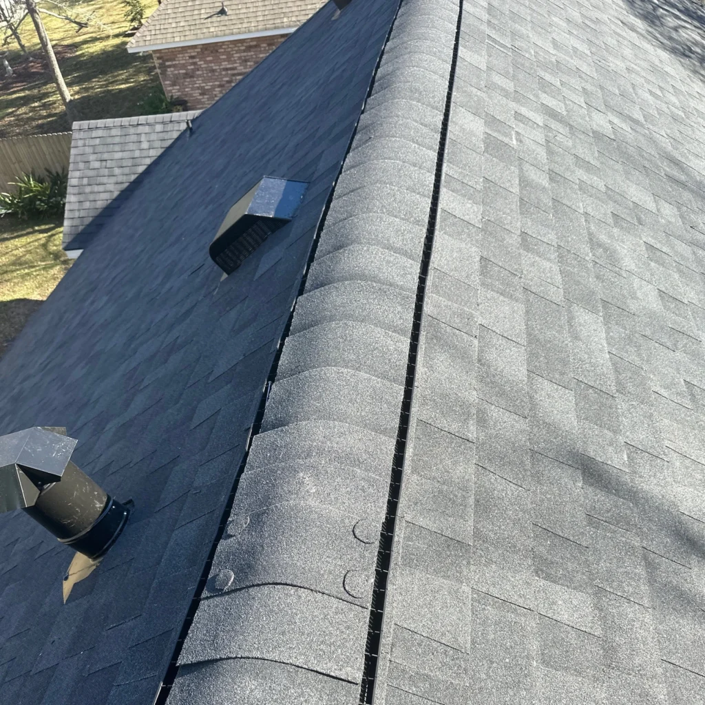 Dark gray Owens Corning Onyx Black architectural shingles on large fortified residential roof with ridge vent and metal roof vents.