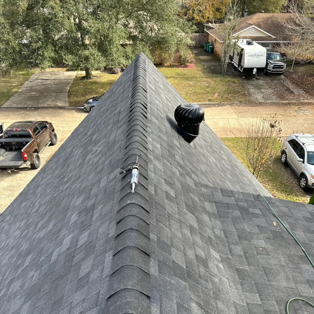 Dark gray OC Duration Onyx Black shingles on steep residential hip roof ridge with turbine vent, Slidell LA neighborhood