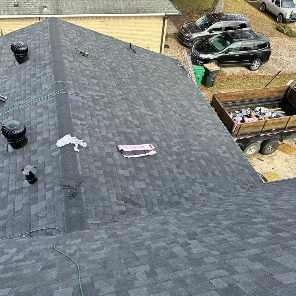 Aerial view of completed large residential fortified roof replacement with OC Onyx Black shingles, vents, and debris trailer visible.