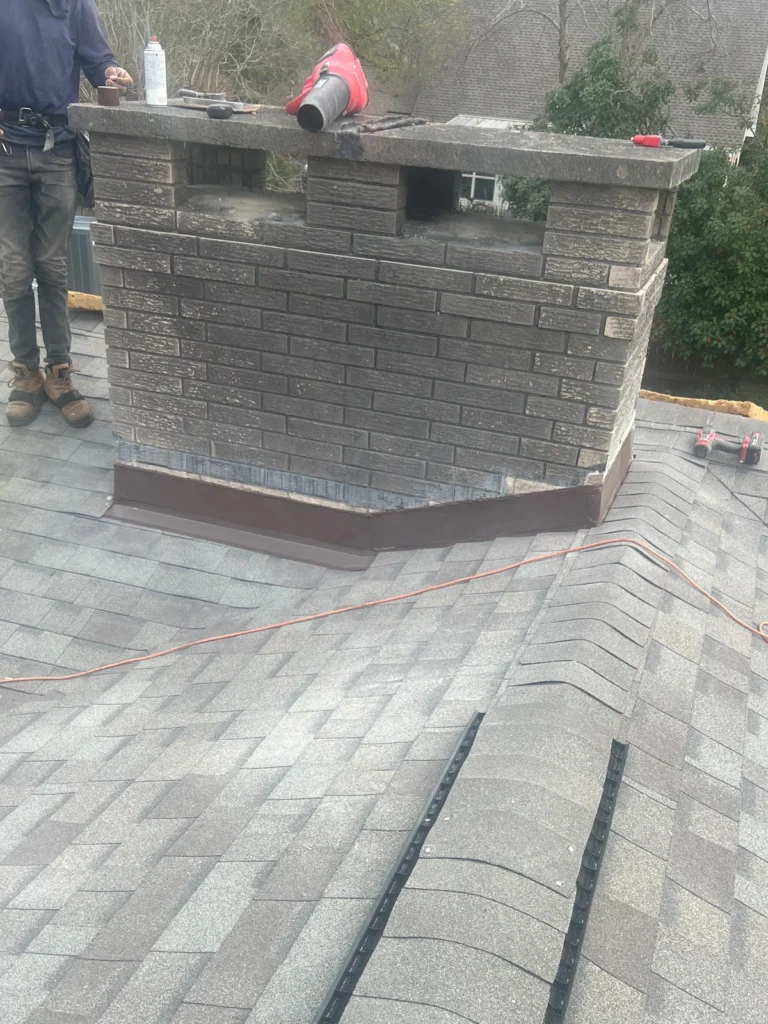 Brick chimney with new brown metal flashing on replaced OC Driftwood asphalt shingle roof, Slidell residential project.
